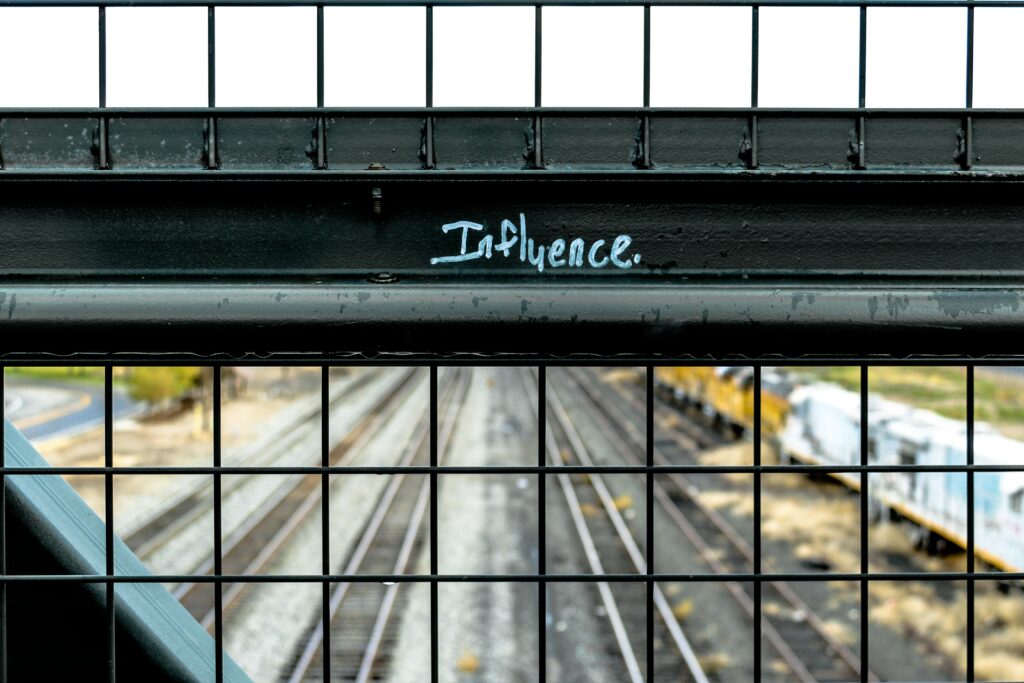 A fence at the side of bridge over a motorway, with the word 'Influence' written on it